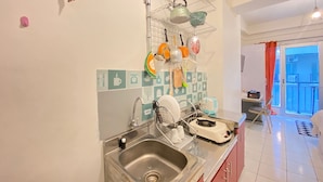 Una cocina con un lavamanos de acero inoxidable, un escurreplatos y una tetera colgada en una repisa de alambre.