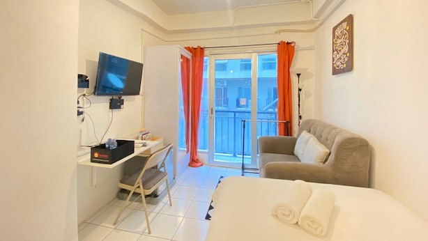 Un dormitorio con cama, escritorio y silla, televisor y balcón con cortinas naranjas.