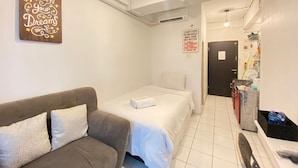 Habitación de hotel con cama, sofá, letrero en la pared, puerta y zona de kitchenette.
