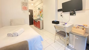 Una habitación de hotel con una cama, un escritorio con silla, televisión y kitchenette.