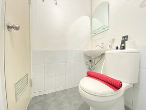 A bathroom with a white toilet, a sink, and a mirror. - Cozy Studio Room at Grand Asia Afrika Apartment (Bandung)