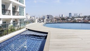 Une piscine sur le toit offrant une vue sur la ville, une zone de baignade carrelée et un immeuble doté de balcons.