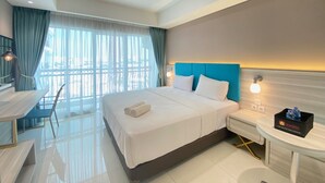 Une chambre d’hôtel avec un grand lit, un bureau et une chaise. Il y a une fenêtre avec des rideaux, une table de chevet avec une lampe et une petite table sur laquelle se trouve un plateau avec des articles de toilette.