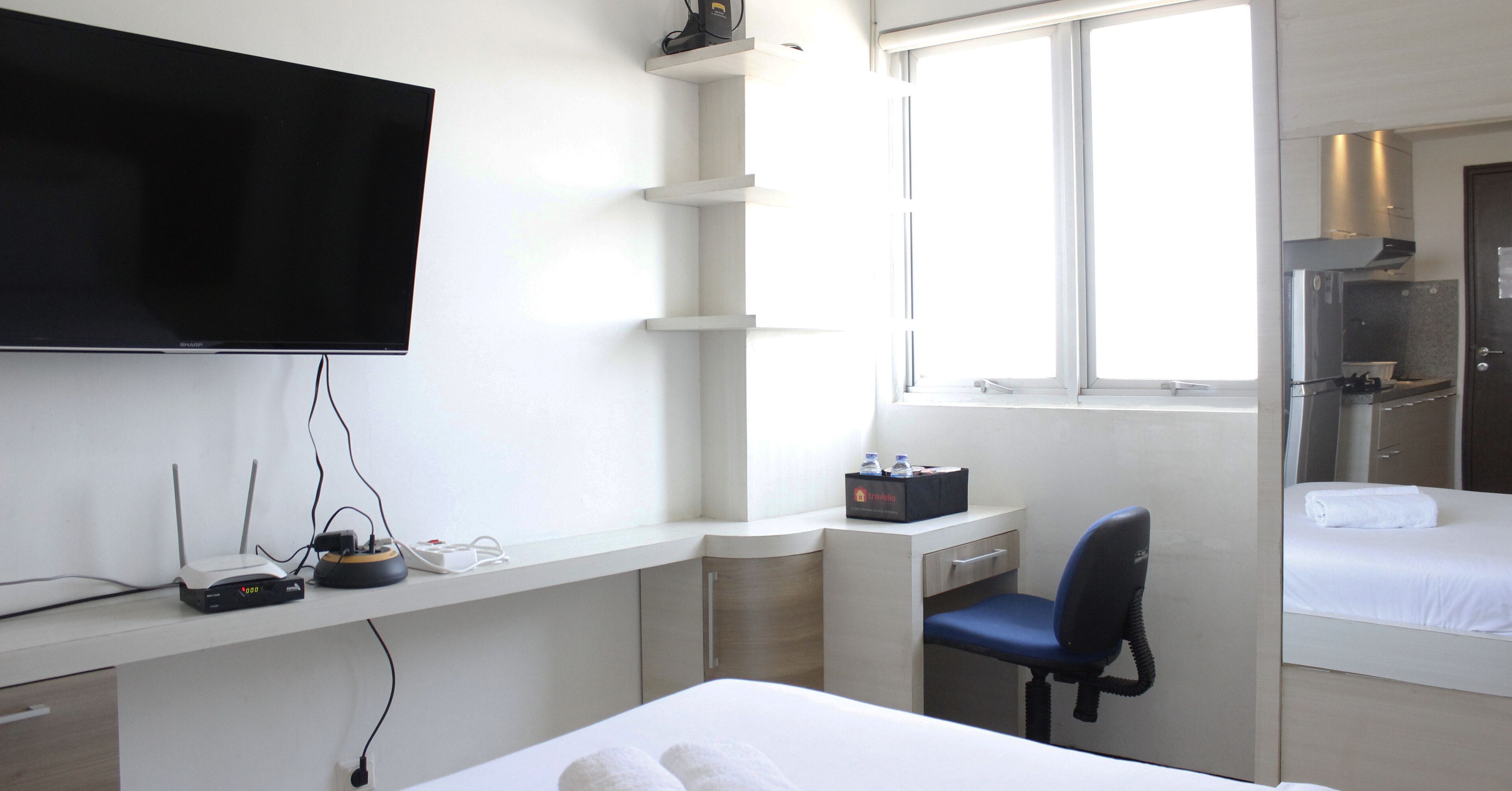 Une chambre d’hôtel comprenant un lit, un bureau avec un ordinateur, une chaise, un téléviseur fixé au mur et une fenêtre.
