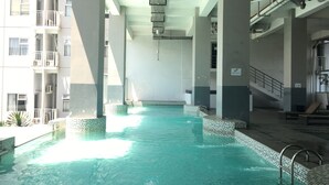 An indoor swimming pool with tiled edges, surrounded by a high-rise building with balconies and staircases. - Nice View Studio Apartment at Harvard Jatinangor near IPDN (Cileunyi)
