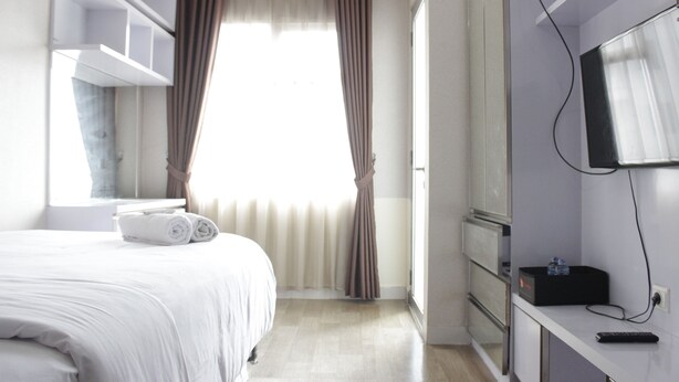 A hotel room with a bed, a TV, a desk, and a window with curtains. - Nice View Studio Apartment at Harvard Jatinangor near IPDN (Cileunyi)