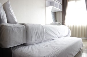 Una cama bien hecha con sábanas blancas y una toalla enrollada en la cabecera.