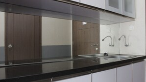 A modern kitchen with a black countertop, stainless steel sink, and wooden cabinets. - Nice View Studio Apartment at Harvard Jatinangor near IPDN (Cileunyi)
