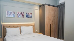 A neatly made bed with white linens and a folded towel, a wooden headboard, and two abstract paintings on the wall. - Comfortable and Homey 2BR Apartment at M-Town Residence (Gading Serpong)