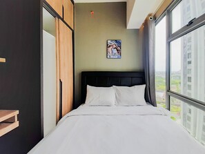 Moderni hotellihuone, jossa on suuri sänky, puinen vaatekaappi, taulu seinällä ja näkymä rakennuksiin ikkunasta.