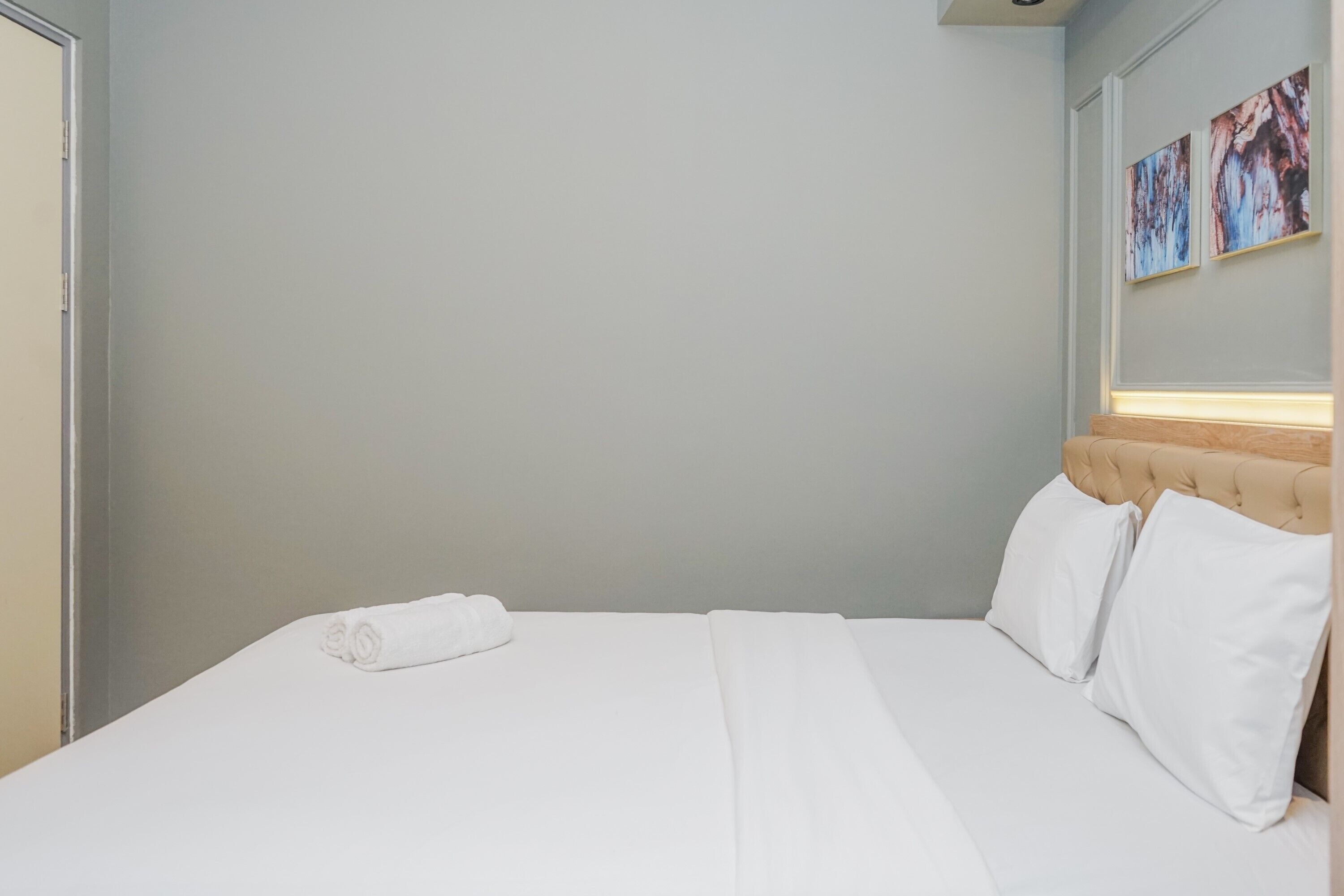 A hotel room with a neatly made bed, a headboard with a light-colored upholstered panel, and two wall-mounted paintings.