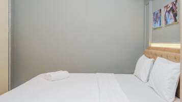 A hotel room with a neatly made bed, a headboard with a light-colored upholstered panel, and two wall-mounted paintings.