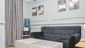 A modern living room with a grey sofa, a coffee table, and a water dispenser. - Comfortable and Homey 2BR Apartment at M-Town Residence (Gading Serpong)