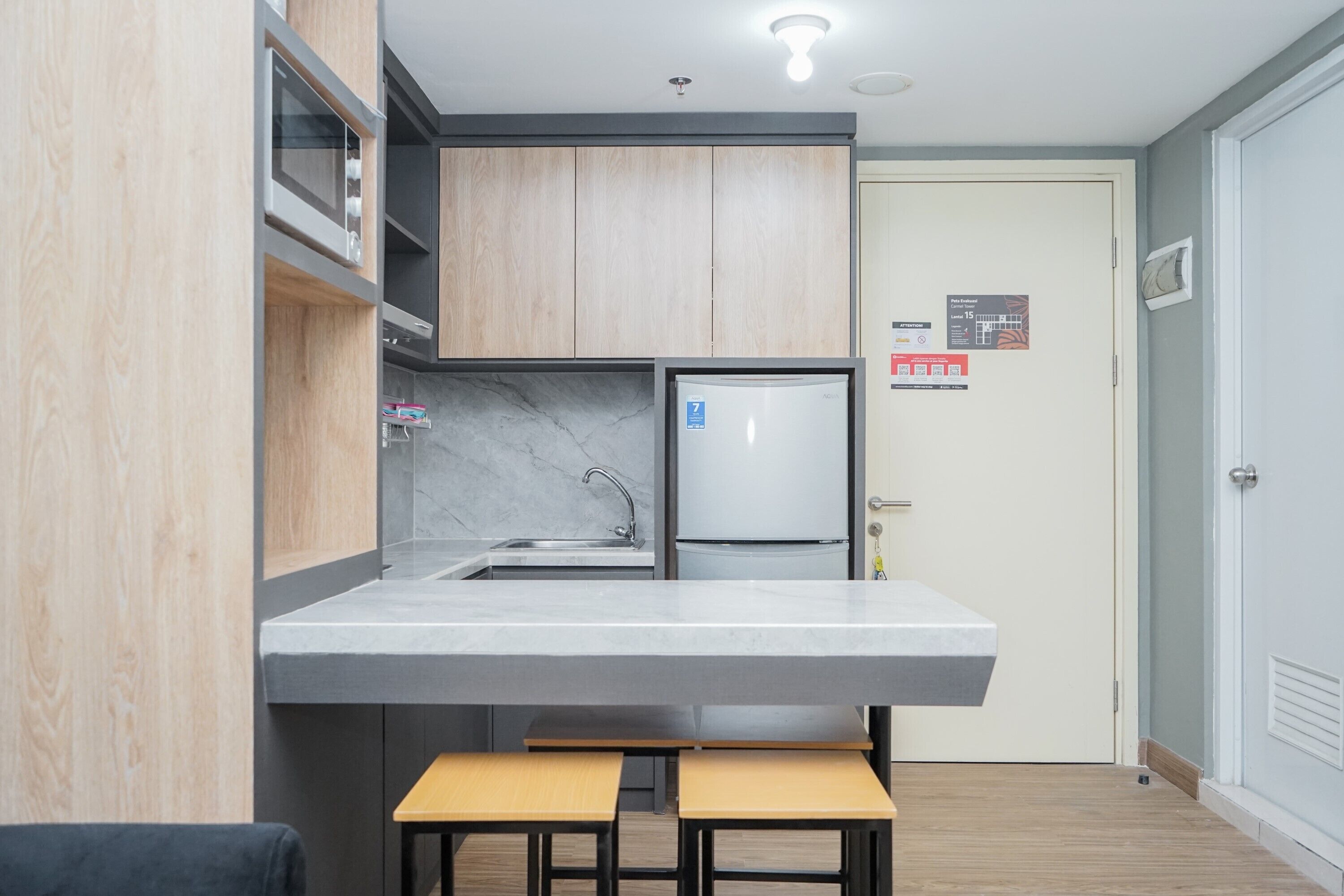 Cocina compacta con lavamanos integrado, refrigerador y armarios de madera. Hay dos taburetes en la encimera.