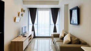 Ein modernes Wohnzimmer mit Flachbildfernseher, einer Holzunterhaltungsecke, einem beigefarbenen Sofa und einem großen Fenster mit Vorhängen.