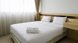 Una cama bien hecha con ropa de cama blanca y una toalla doblada, un cabecero de madera y una mesita de noche con toma de corriente.