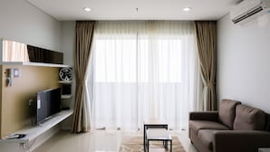 Un salón moderno con un televisor de pantalla plana, un sofá, una mesita y cortinas traslúcidas.