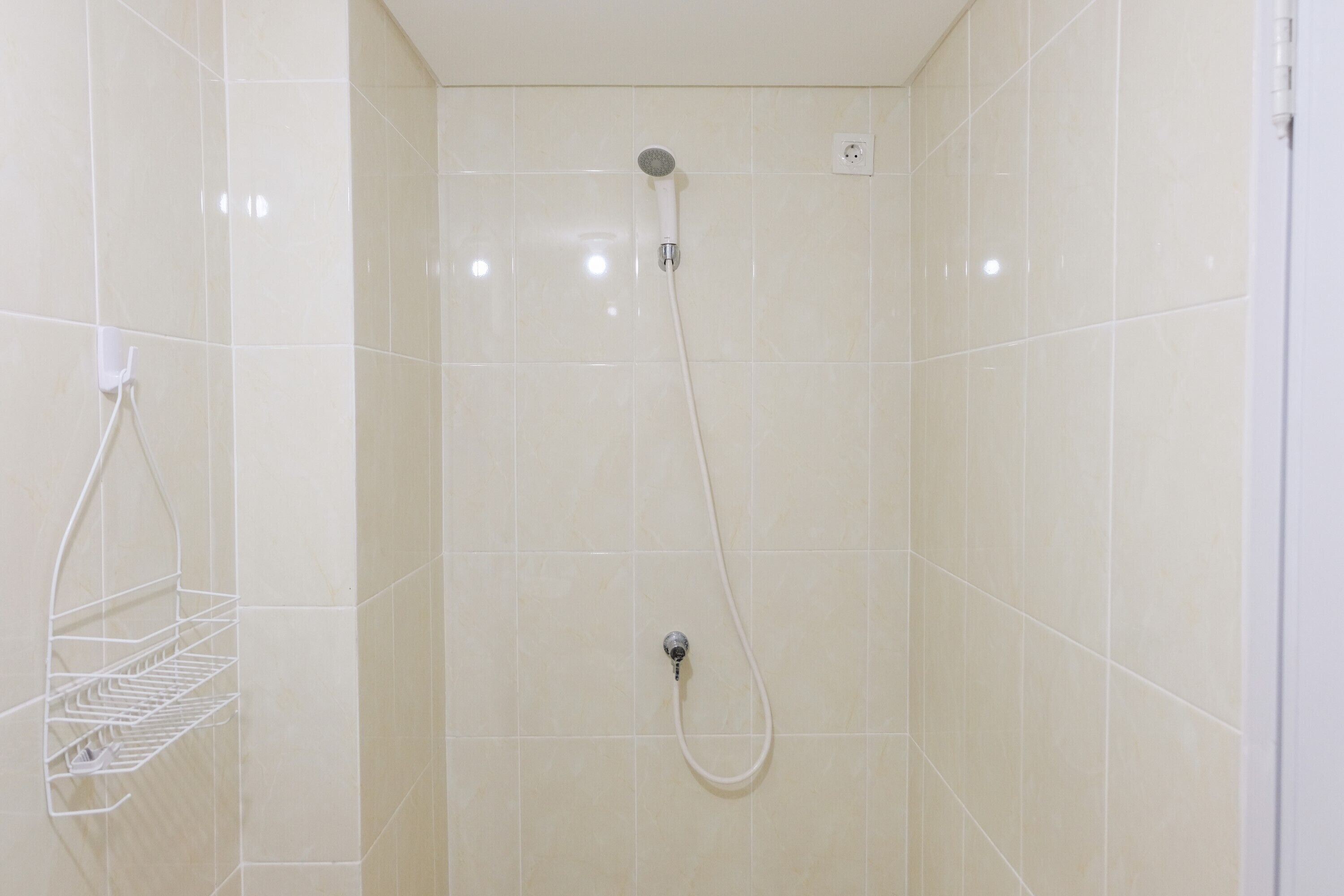 Eine Dusche mit Handbrause und Wandarmatur, ein weißer Handtuchhalter und eine Steckdose an der Wand.