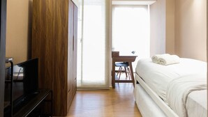 A bedroom with a bed, a wooden wardrobe, a desk, and a television. - Studio Room Apartment at M-Town Residence near Summarecon Mall Serpong (Gading Serpong)