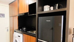A compact kitchen with a washing machine, a Panasonic refrigerator, and wooden cabinets. - Studio Room Apartment at M-Town Residence near Summarecon Mall Serpong (Gading Serpong)