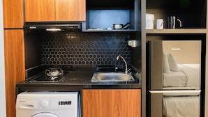 A compact kitchen with wooden cabinets, a black countertop, a built-in stove, a sink, and a refrigerator. - Studio Room Apartment at M-Town Residence near Summarecon Mall Serpong (Gading Serpong)