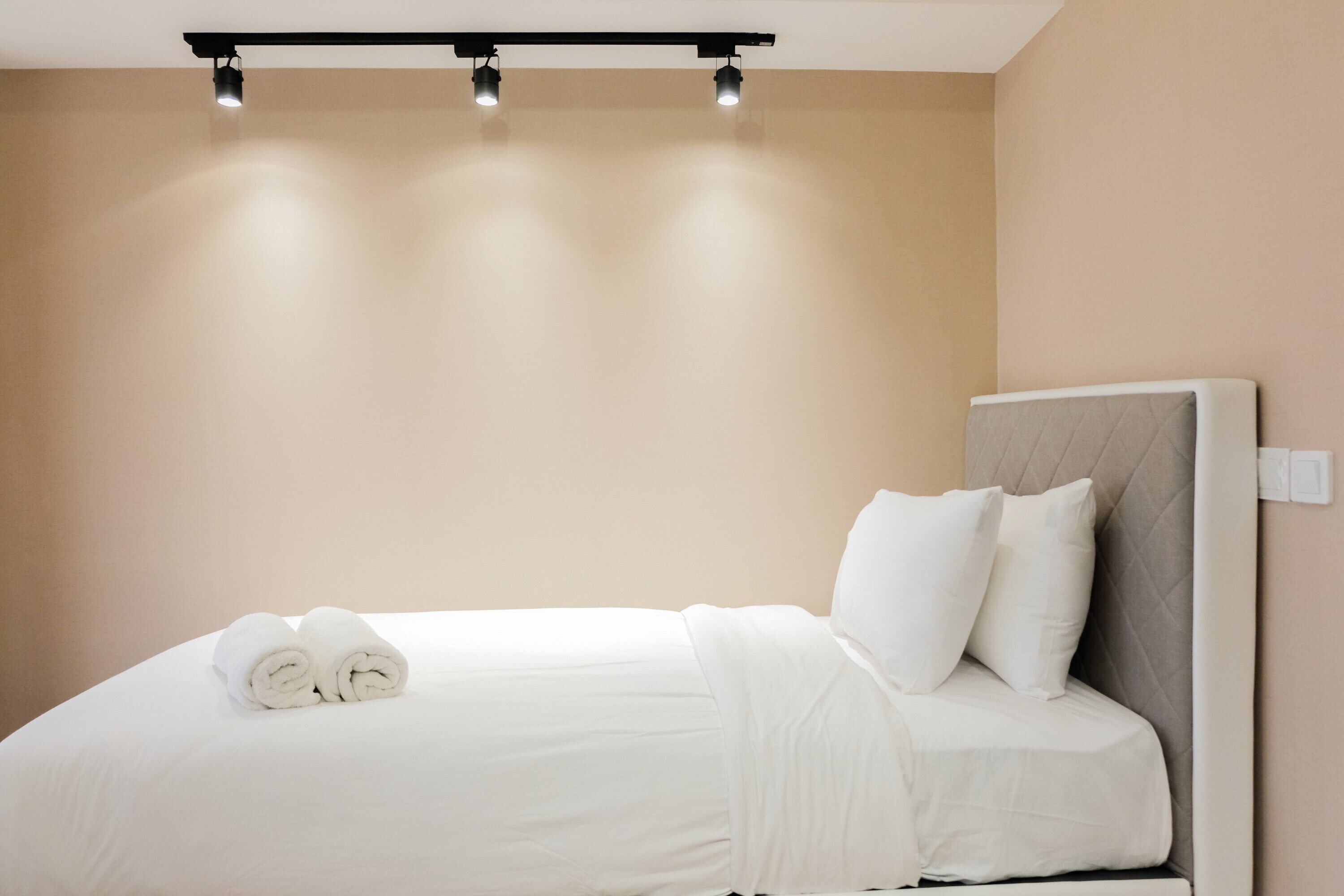 A neatly made bed with white linens and rolled towels, a headboard, and three ceiling lights.