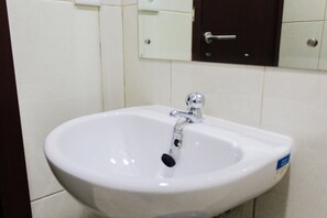 A white bathroom sink with a chrome faucet, a mirror above it, and a dark-colored cabinet with a silver handle. - Cozy 1BR at Asatti Apartment (Pagedangan)
