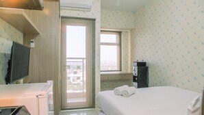 A hotel room with a bed, a TV, a desk with a computer, a window, and a door leading outside. - Modern Furnished Studio at Springlake Summarecon Bekasi Apartment (Bekasi)