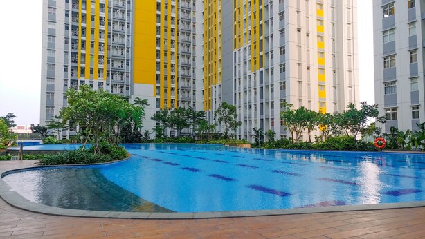 A swimming pool surrounded by greenery and tall residential buildings with balconies. - Modern Furnished Studio at Springlake Summarecon Bekasi Apartment (Bekasi)