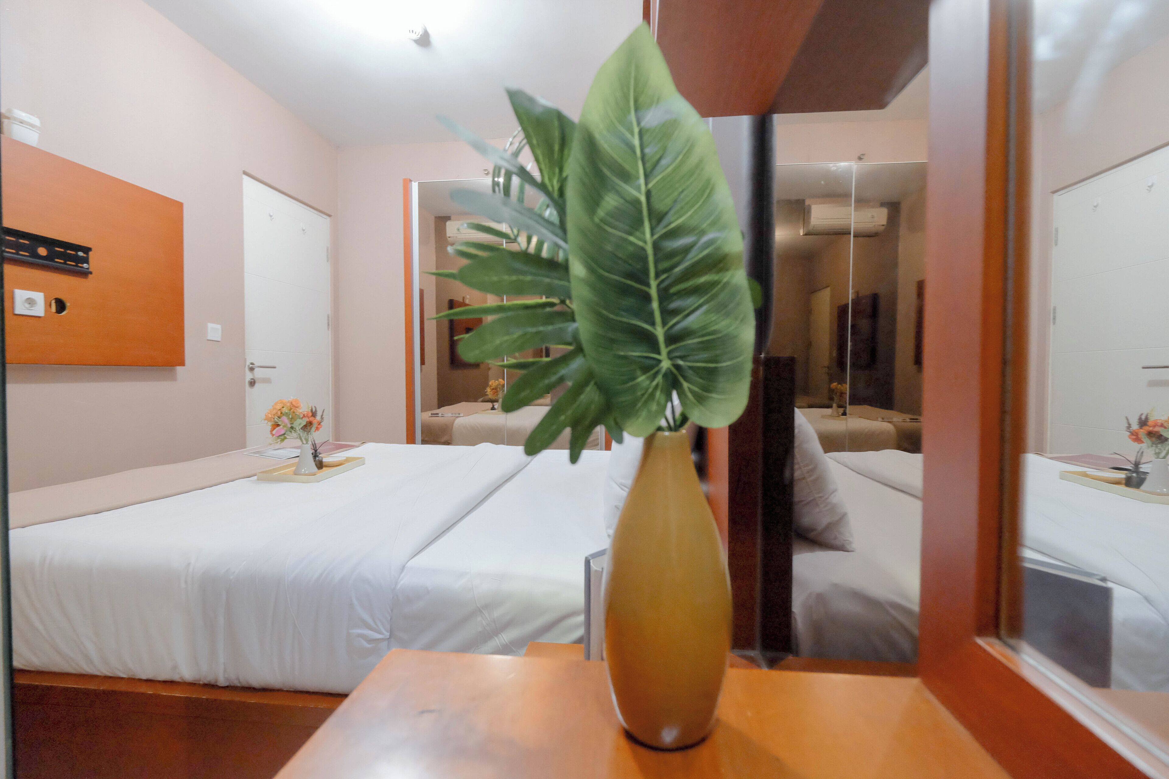 Une chambre d’hôtel avec deux lits simples, une table en bois ornée d’un vase et un grand miroir qui reflète la pièce.