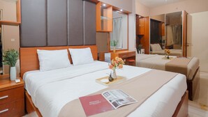 A hotel room with a large bed, a desk, a mirror, and a small table with a vase of flowers. - Modern 2BR Apartment for 4 Pax at Springlake Summarecon (Bekasi)