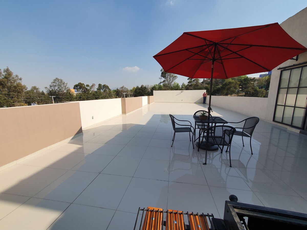 A rooftop patio with a red umbrella, a table, and chairs.