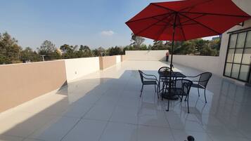A rooftop patio with a red umbrella, a table, and chairs.