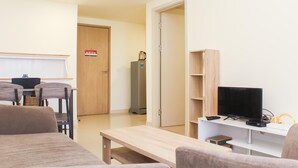 A modern living room with a sofa, a coffee table, a TV, and a dining area with chairs and a table. - Spacious and Well Appointed 2BR at Meikarta Apartment (Cikarang)