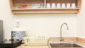 A kitchen with a sink, a kettle, a dish rack, and a shelf with cups and a kettle. - Spacious and Well Appointed 2BR at Meikarta Apartment (Cikarang)