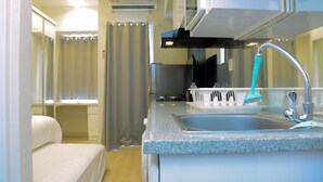 A compact kitchen with a sink, a faucet, and a window with curtains. - Modern and Full Parquette @ Studio Springlake Summarecon Apartment (Bekasi)