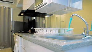 A kitchen with a stainless steel refrigerator, a microwave, a sink with a faucet, and a dish rack. - Modern and Full Parquette @ Studio Springlake Summarecon Apartment (Bekasi)