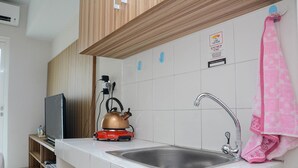 Una cocina con un lavamanos de acero inoxidable, un hervidor y un televisor sobre una repisa de madera.