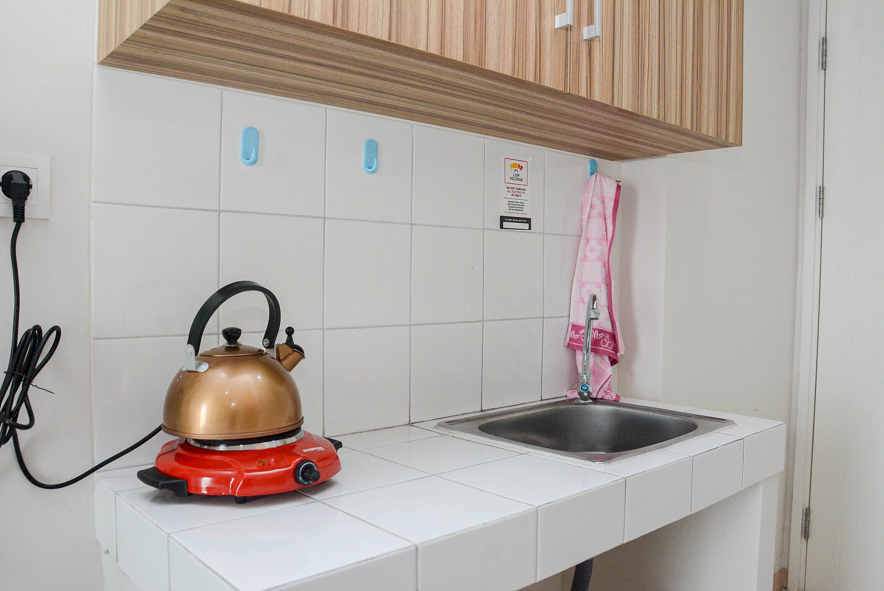 A kitchen with white tiles, a red kettle, a sink, and a wooden cabinet above.