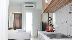 Habitación de hotel compacta con cama, kitchenette, lavamanos y aire acondicionado.