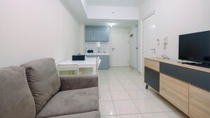 A modern living room with a sofa, a TV, and a kitchen in the background. - Beautiful and Cozy 2BR at Springlake Summarecon Bekasi Apartment (Bekasi)
