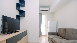 A modern living room with a flat-screen TV on a wooden console, a grey sofa, and a white refrigerator. - Beautiful and Cozy 2BR at Springlake Summarecon Bekasi Apartment (Bekasi)