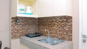 A compact kitchen with a granite countertop, a stainless steel sink, and a backsplash made of small, square tiles. - Gorgeous 2BR Springlake Summarecon Apartment (Bekasi)