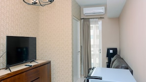 A room with a flat-screen TV on a wooden cabinet, an air conditioning unit on the wall, a ceiling light fixture, and a sliding door leading to a balcony. - Gorgeous 2BR Springlake Summarecon Apartment (Bekasi)