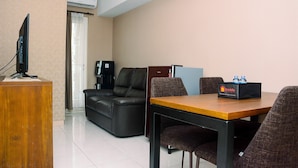 A hotel room with a wooden desk, a television, a sofa, and a dining table with chairs. - Gorgeous 2BR Springlake Summarecon Apartment (Bekasi)
