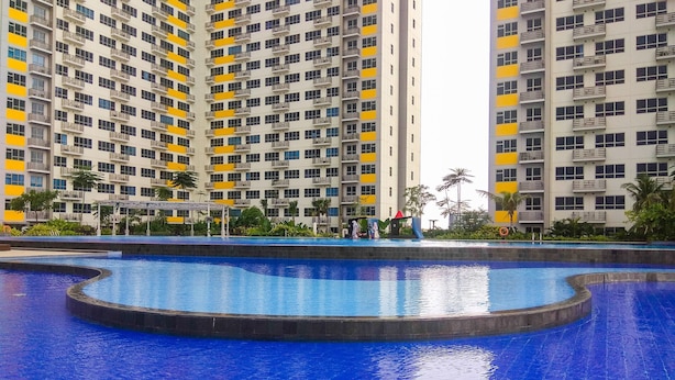 A large swimming pool with a curved design, surrounded by high-rise residential buildings with balconies. - Gorgeous 2BR Springlake Summarecon Apartment (Bekasi)