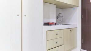 A kitchen with white cabinets, a sink, and a red appliance on the counter. - Cozy Studio at Elvis Tower Apartment (Cikarang)