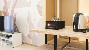 Ett hotellrum med en platt-TV på ett vitt stativ, ett träbord med en svart låda märkt med texten ”Travelio Property Management” och två flaskor, samt en kaffebryggare på bordet.