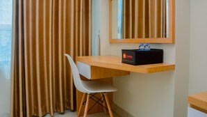 Una habitació d'hotel amb un escriptori de fusta, una cadira blanca, un mirall i una caixa negra etiquetada 'travelio' sobre l'escriptori.