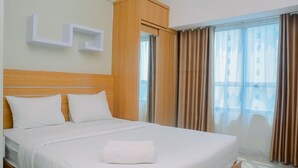 Habitació d'hotel amb un llit gran, un panell de melí amb capçalera, un armari i vista a la ciutat a través de cortines translúcides.